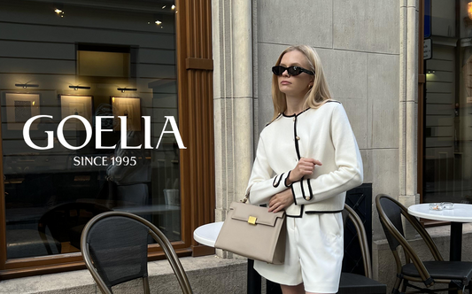 A woman wears a white cardigan and takes a grey bag standing in the street.