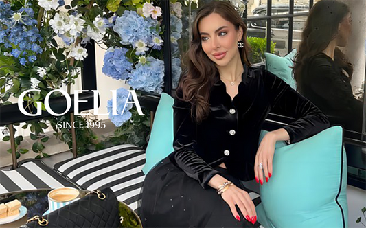 A lady wears a velvet top and sits on the sofa.